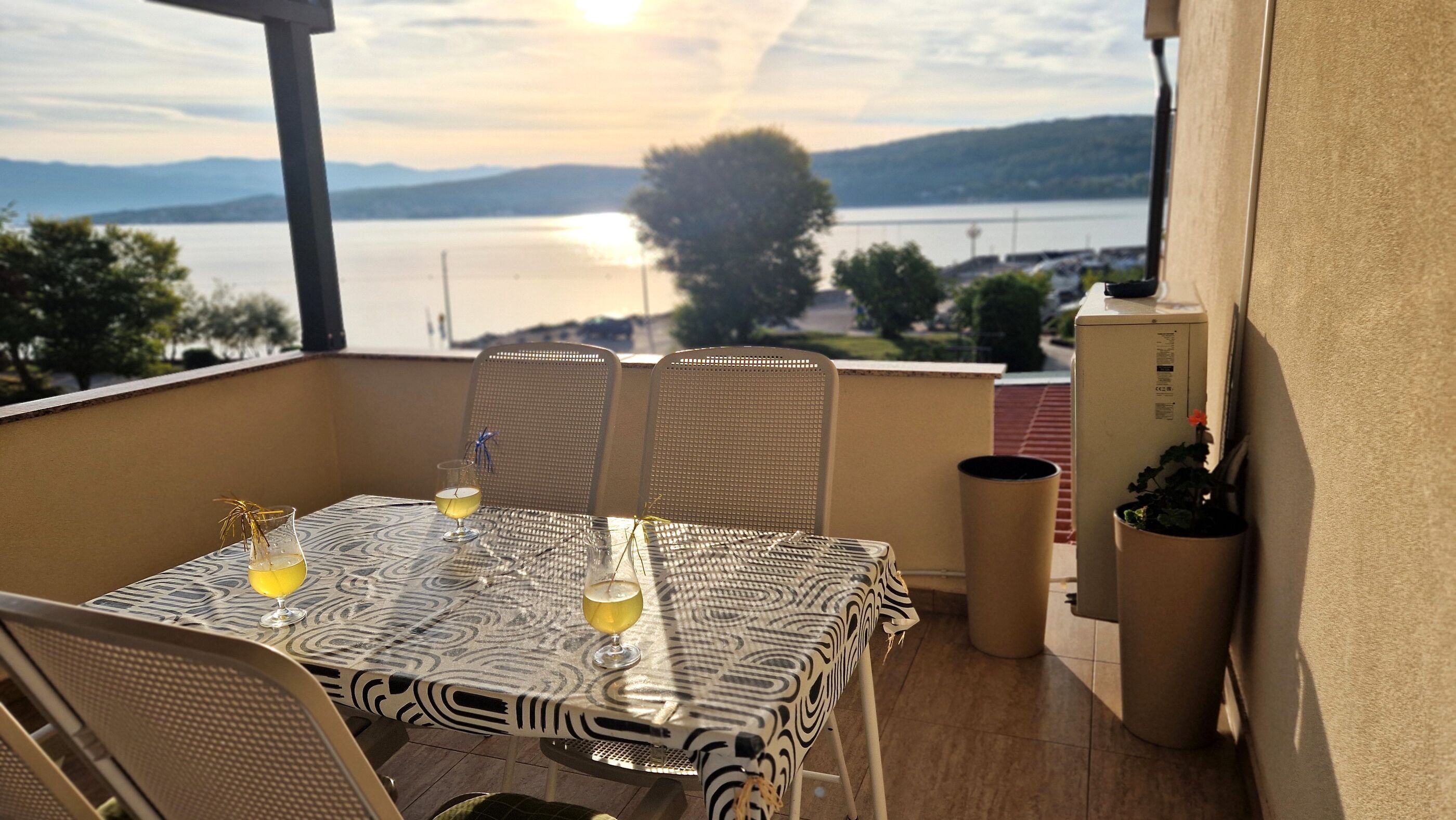 Un balcón con una mesa para dos, con vista a un cuerpo de agua y colinas.