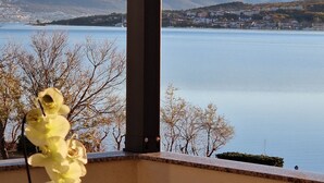 Uma varanda com uma mesa, uma orquídea em vaso e vista para um lago e montanhas ao longe.