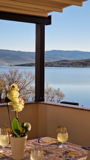 A balcony with a table, a potted orchid, and a view of a lake and distant mountains.
