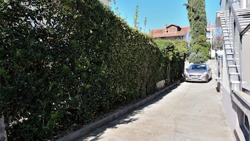 Una calle estrecha con un automóvil estacionado a la derecha, bordeada por edificios y abundante vegetación.