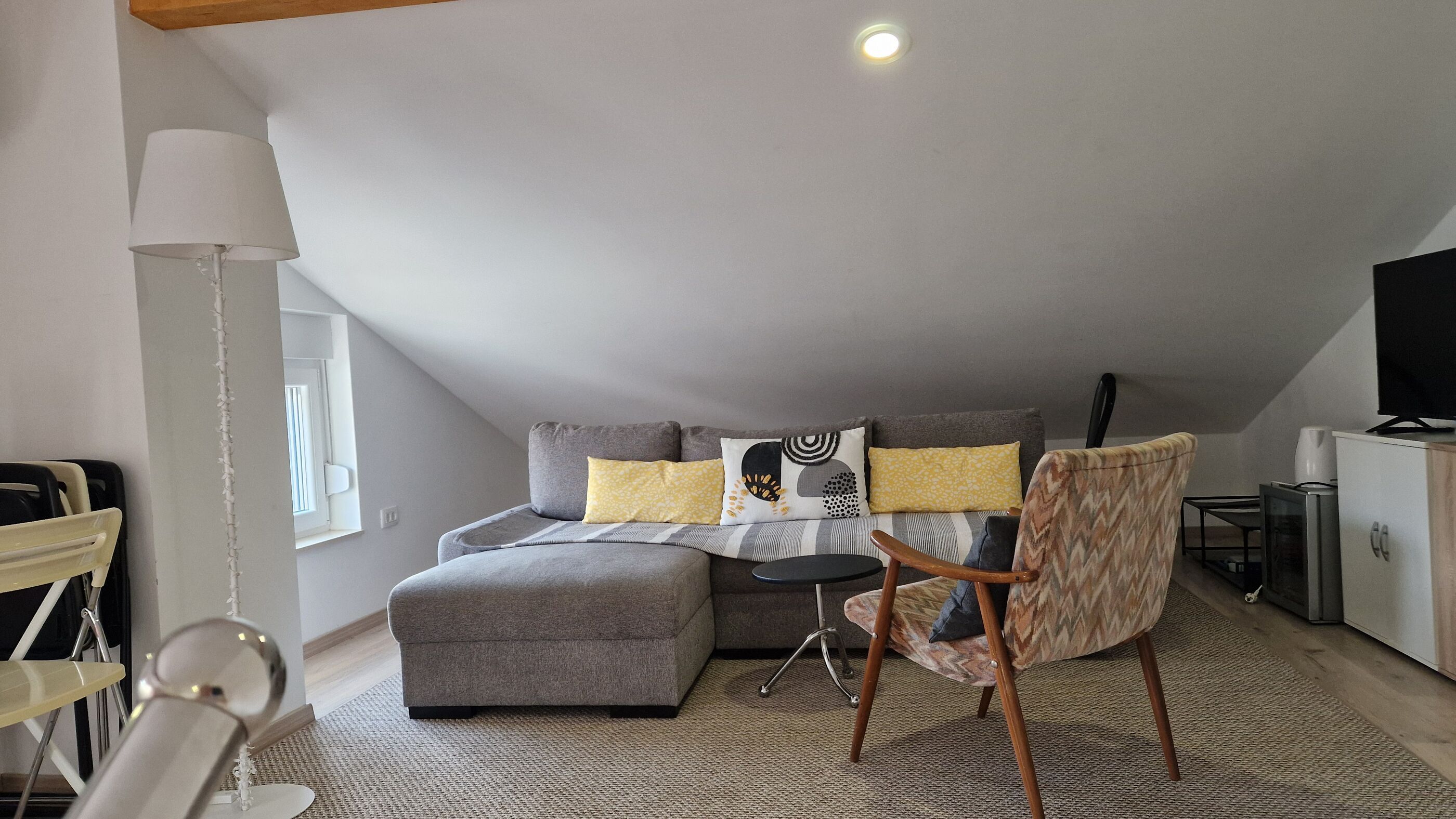 Ein modernes Schlafzimmer im Loft-Stil mit einem grauen Sofa, einem kleinen runden Tisch und einem Sessel.