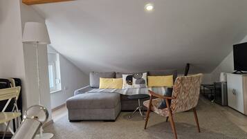 Ein modernes Schlafzimmer im Loft-Stil mit einem grauen Sofa, einem kleinen runden Tisch und einem Sessel.