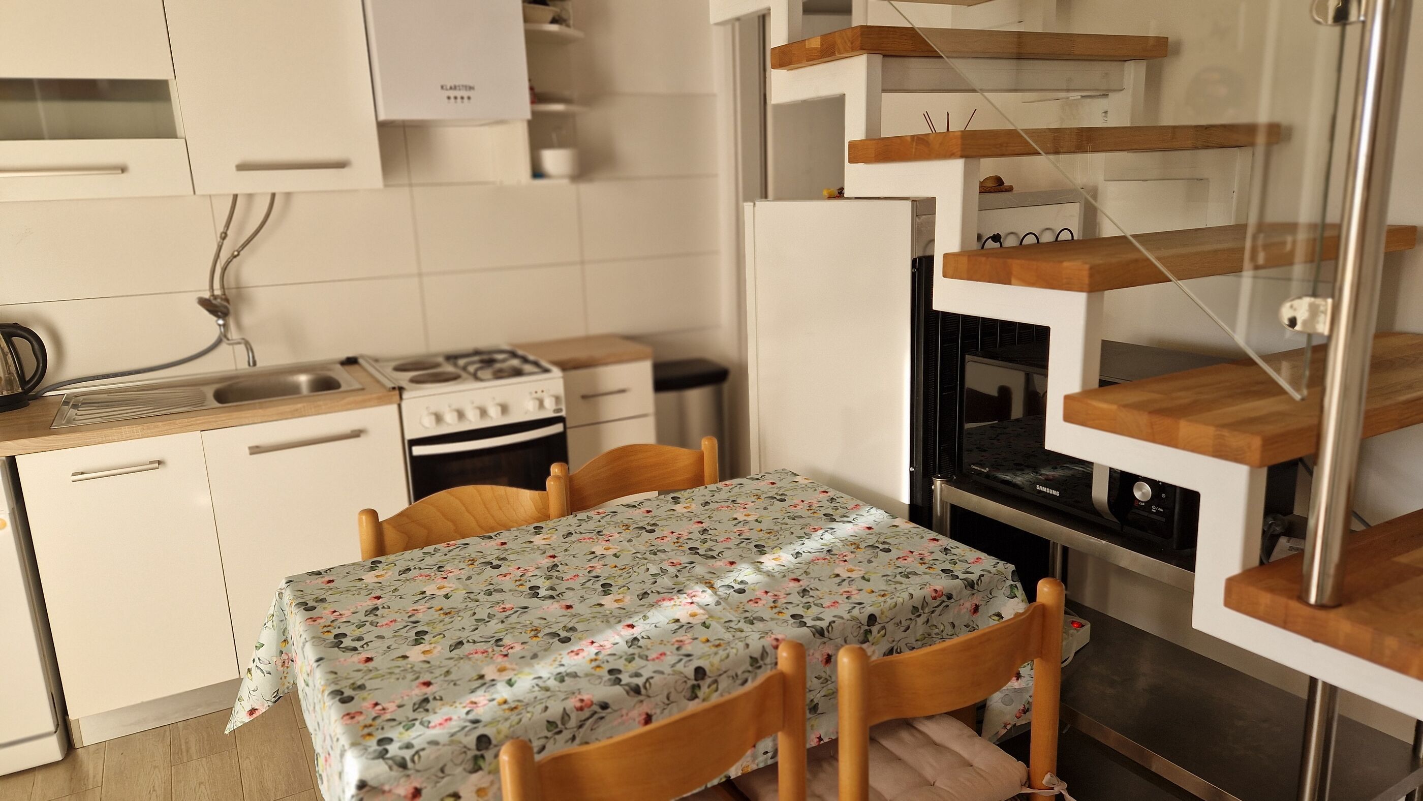 Uma cozinha compacta com armários brancos, fogão e uma mesa de jantar com cadeiras.