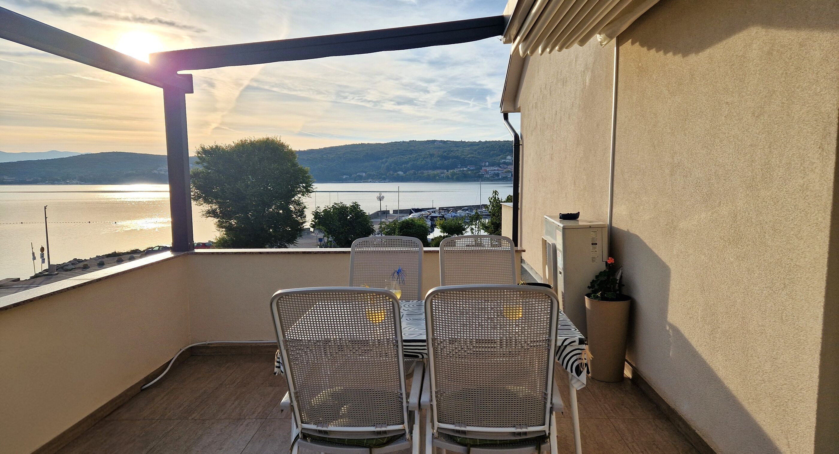 A balcony with a table and chairs, overlooking a body of water and distant landscape.