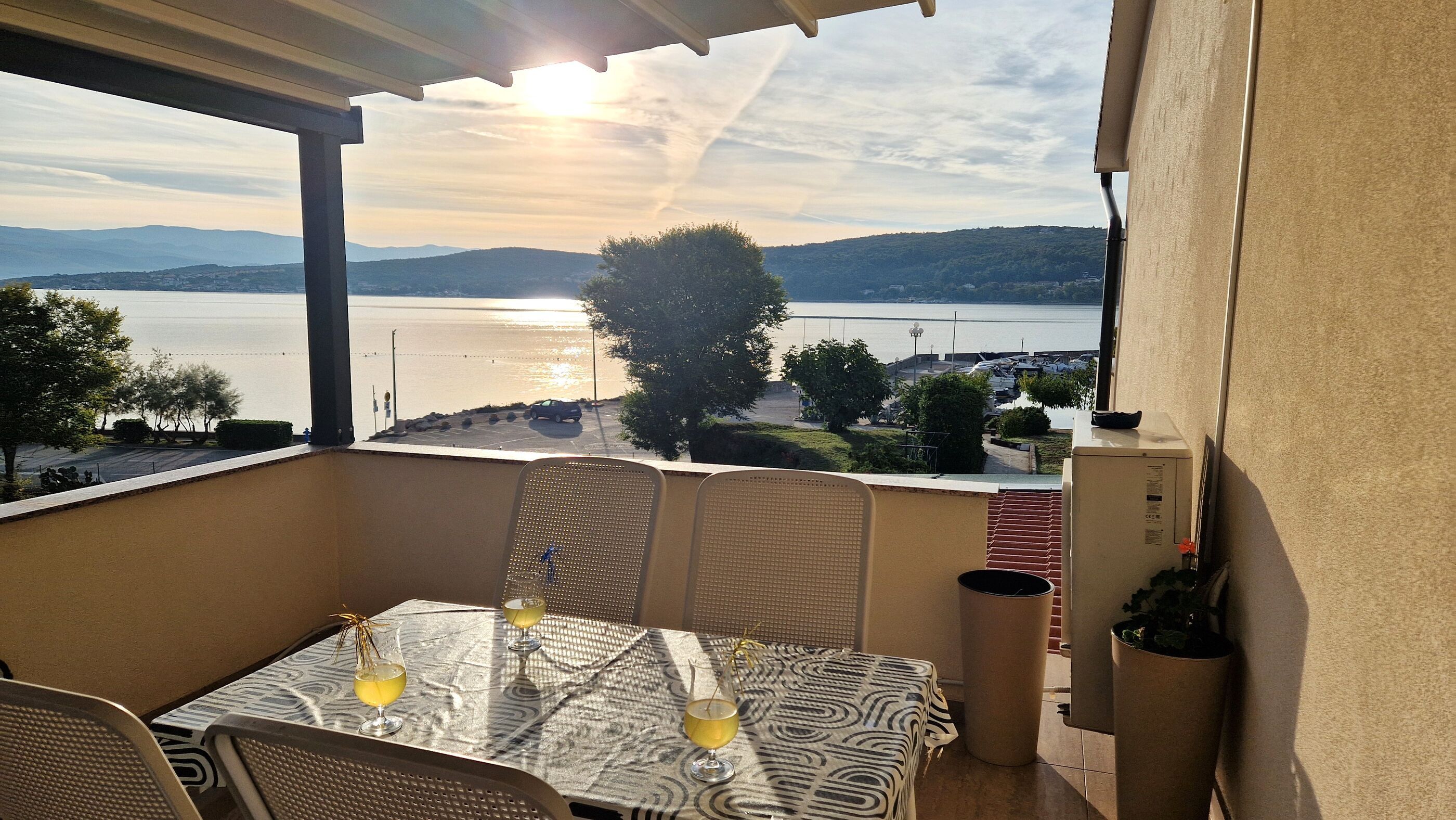 A balcony with a table and chairs, overlooking a body of water and a distant landscape.
