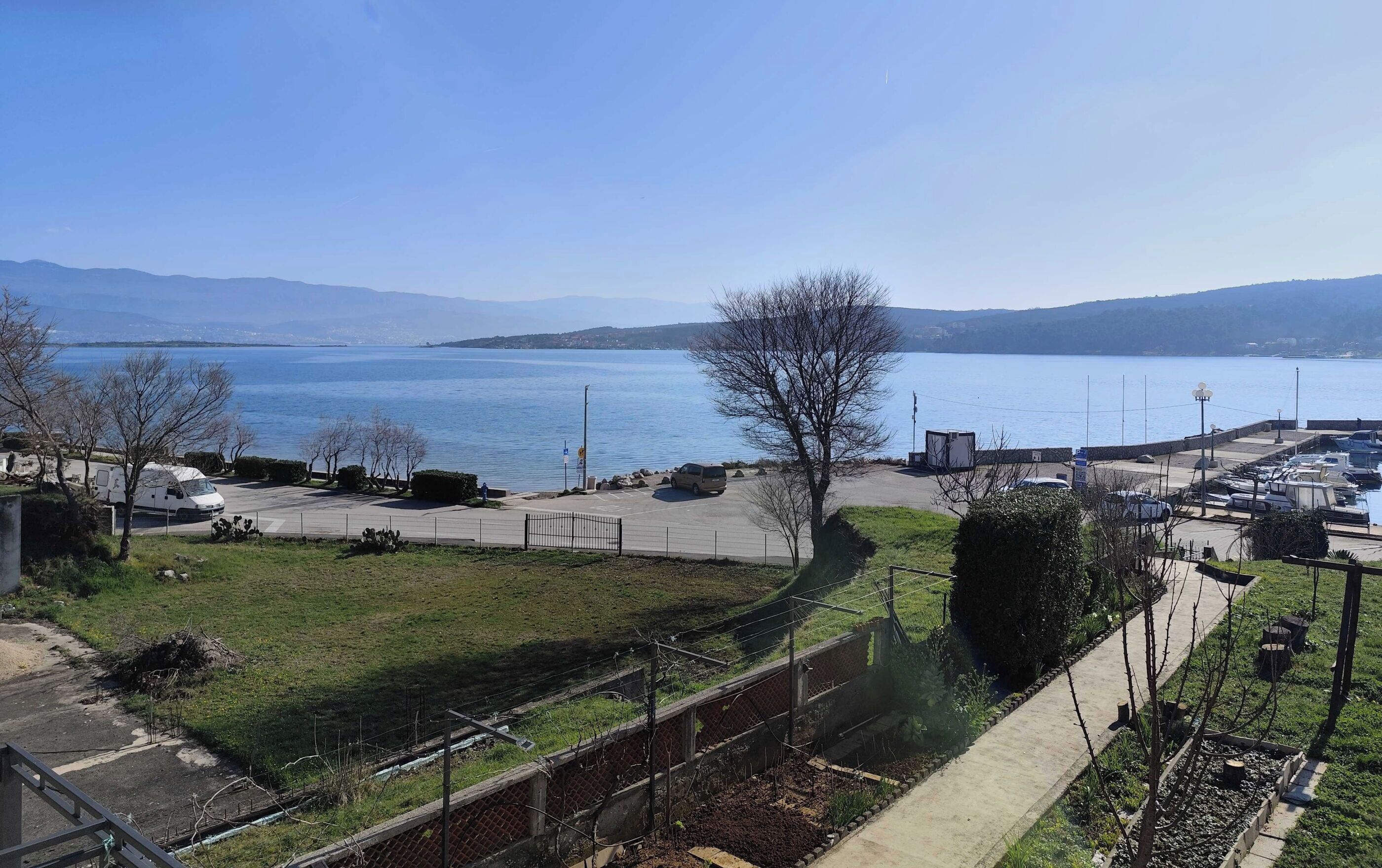 A coastal view with a parking area, a grassy field, and a body of water.
