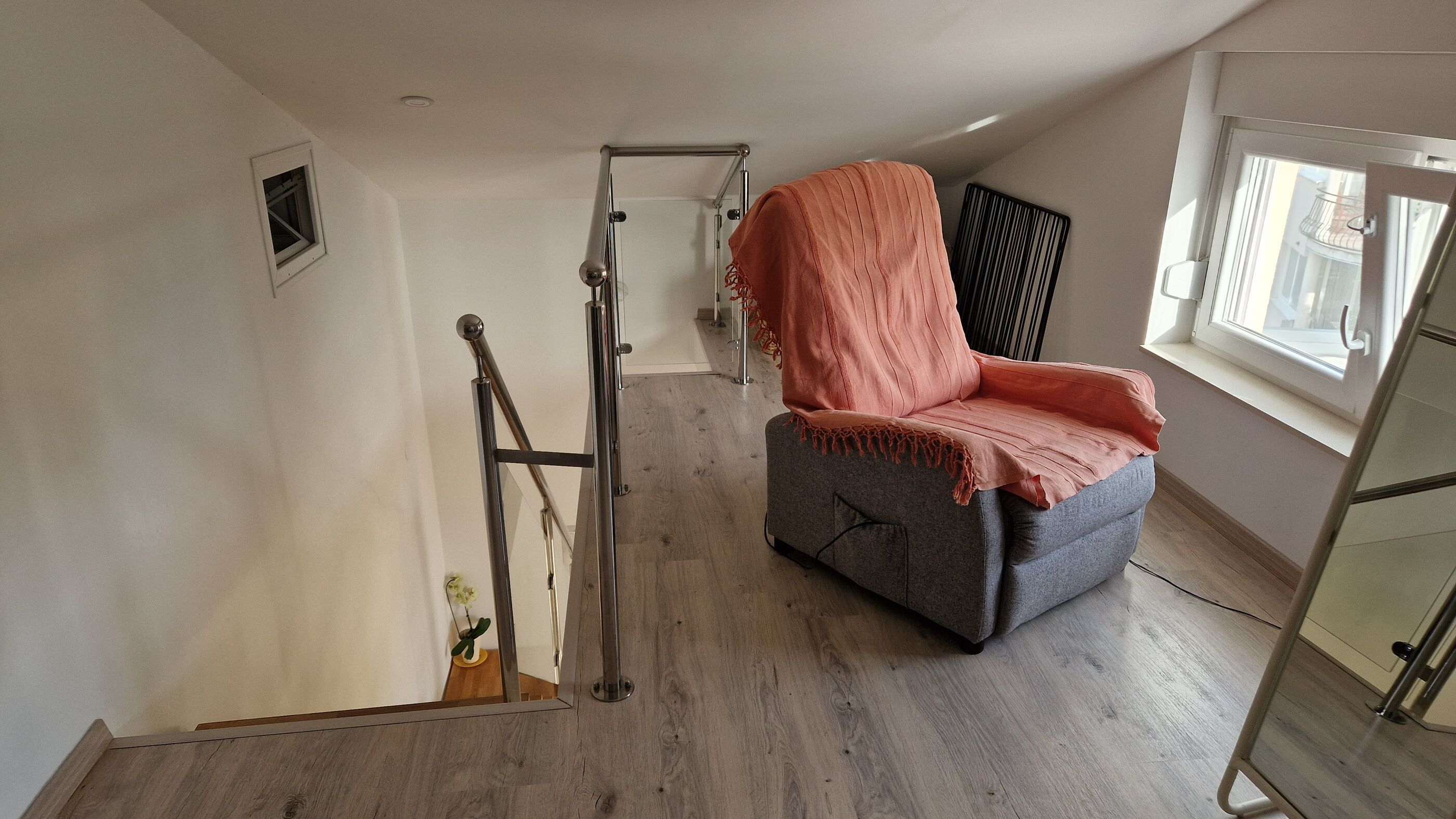 Quarto com sofá cinzento, grade de metal, janela e porta.