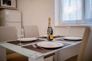 A dining table with a bottle of champagne, two glasses, and plates set for two. - Apartments Lili (Rab)
