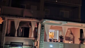 Ein zweistöckiges Gebäude mit Balkon, Bank und Blumentöpfen.