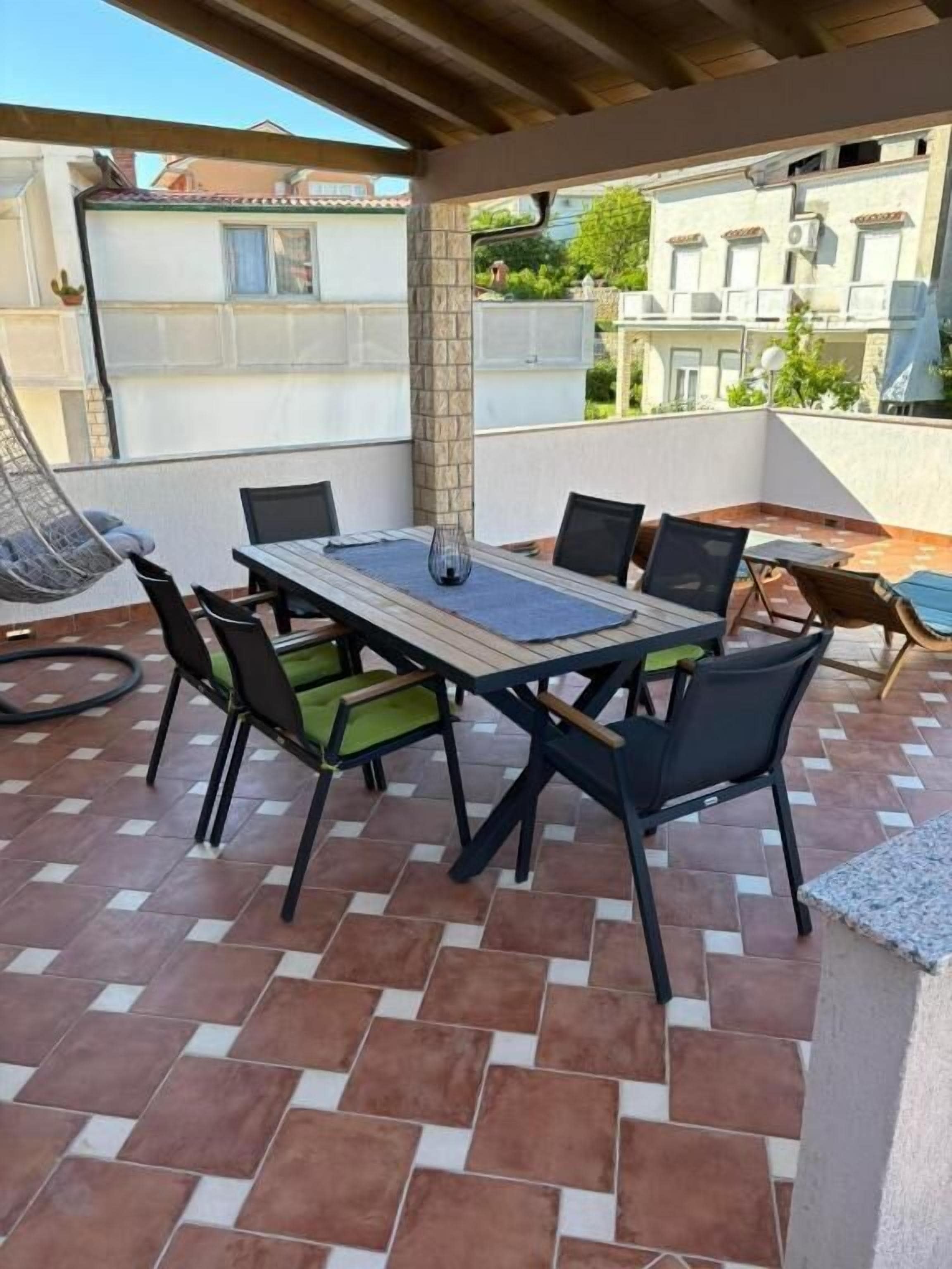 A patio with a table and chairs, a hanging chair, and a view of buildings in the background.