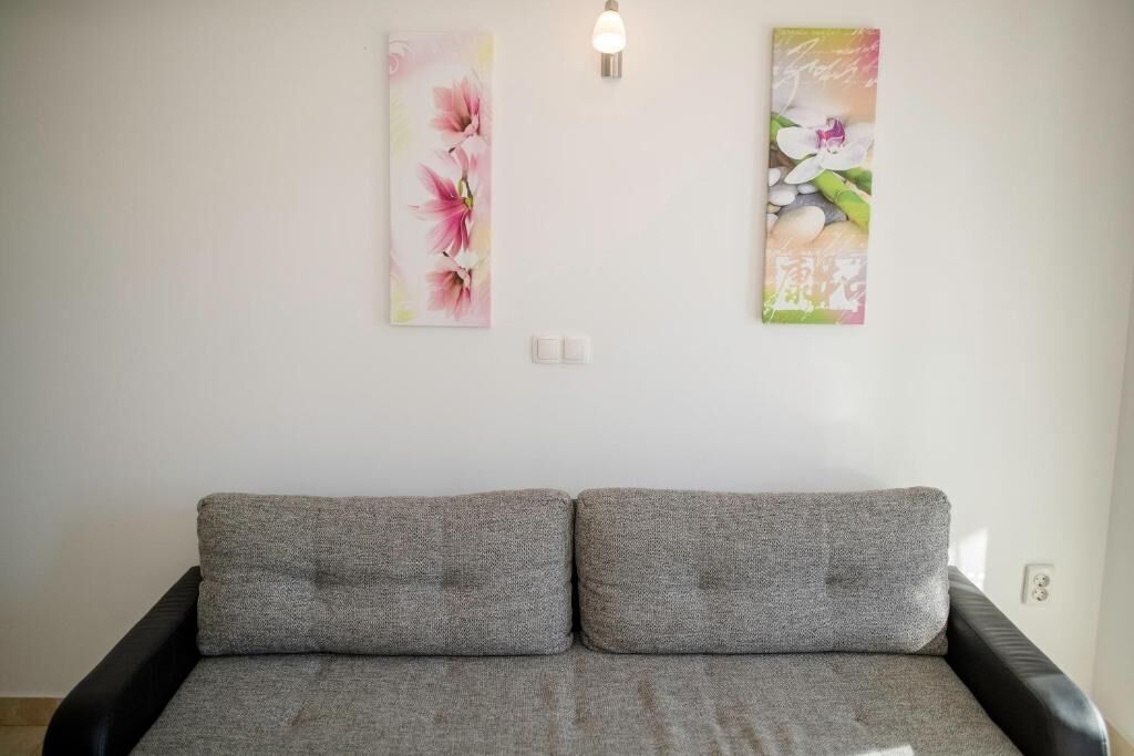 A room with a grey sofa, two wall-mounted light fixtures, and two floral wall art pieces.