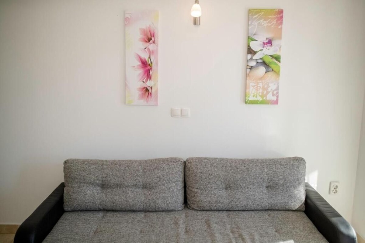Ein Zimmer mit grauem Sofa, zwei Wandleuchten und zwei floralen Wandbildern.