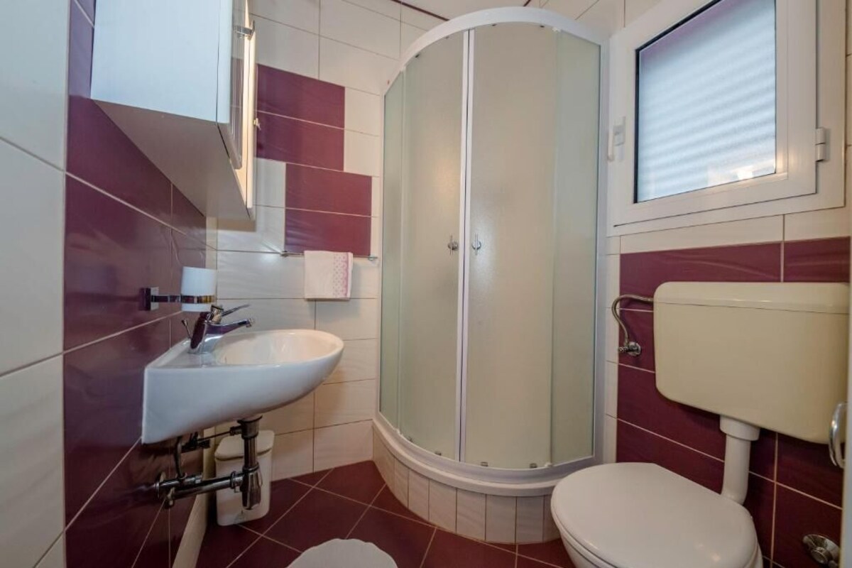 Ein Badezimmer mit Dusche, Waschbecken, Toilette und Fenster.