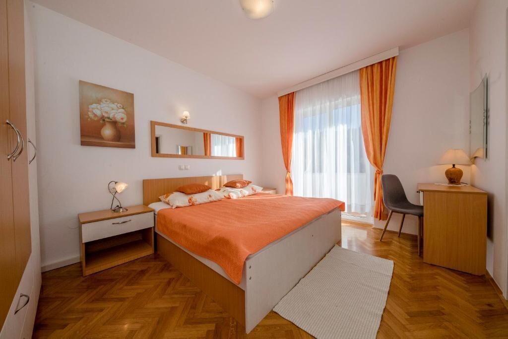 Een slaapkamer met een bed, nachtkastje, lamp, stoel, bureau en een schilderij aan de muur.