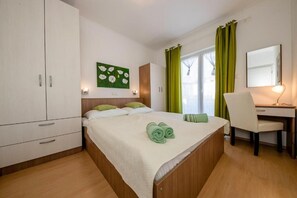 A bedroom with a bed, a desk, a chair, a wardrobe, and a green wall art piece. - Apartments Lili (Rab)