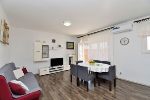 Ein Wohnzimmer mit einer Couch, einem Fernseher, einem Esstisch, Stühlen und einer Wanduhr.