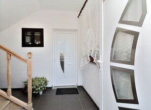 Eine Treppe mit hölzernen Geländern, eine weiße Tür mit Milchglasfenster, ein Blumentopf und eine schwarze Fußmatte am Fuß der Treppe.