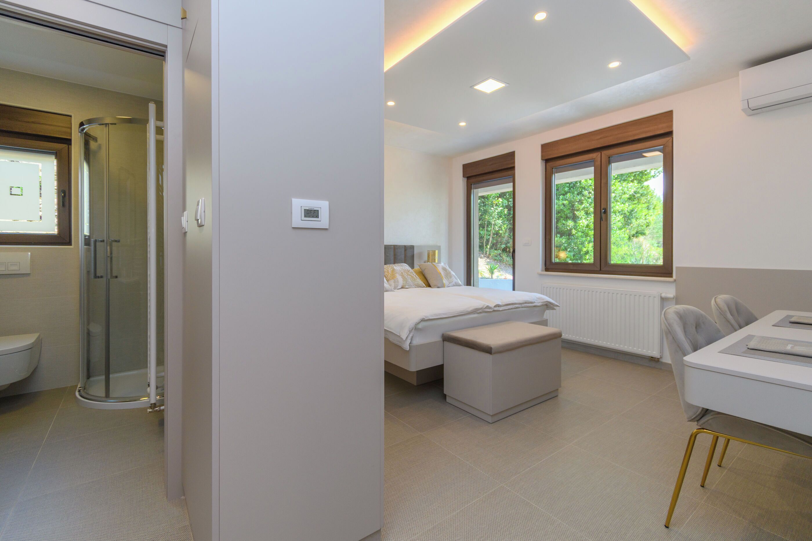A modern hotel room with a shower, a bed, a desk, and large windows.