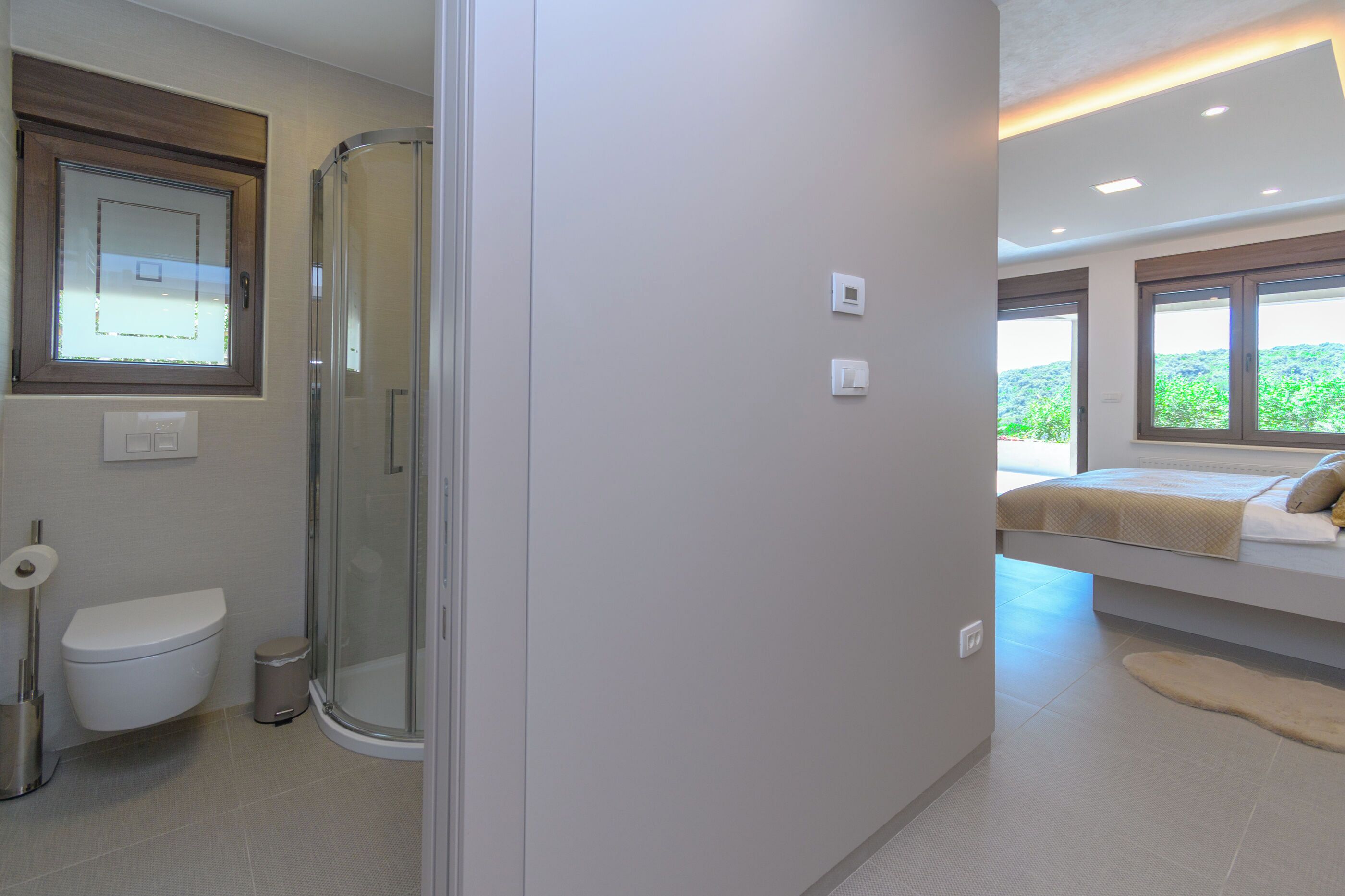 A modern bathroom with a toilet, shower, and a bed with a view.