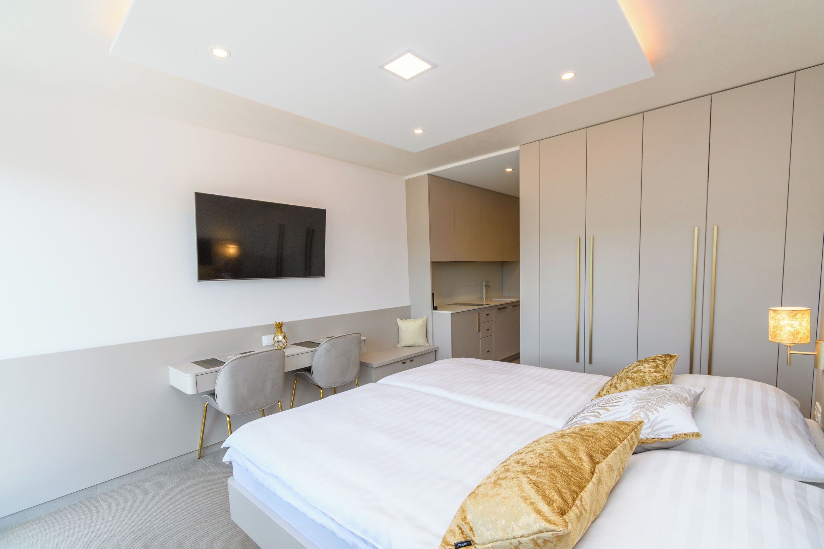 A modern hotel room with a large bed, a desk, and a kitchenette.