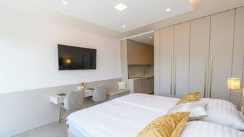 A modern hotel room with a large bed, a desk, and a kitchenette.