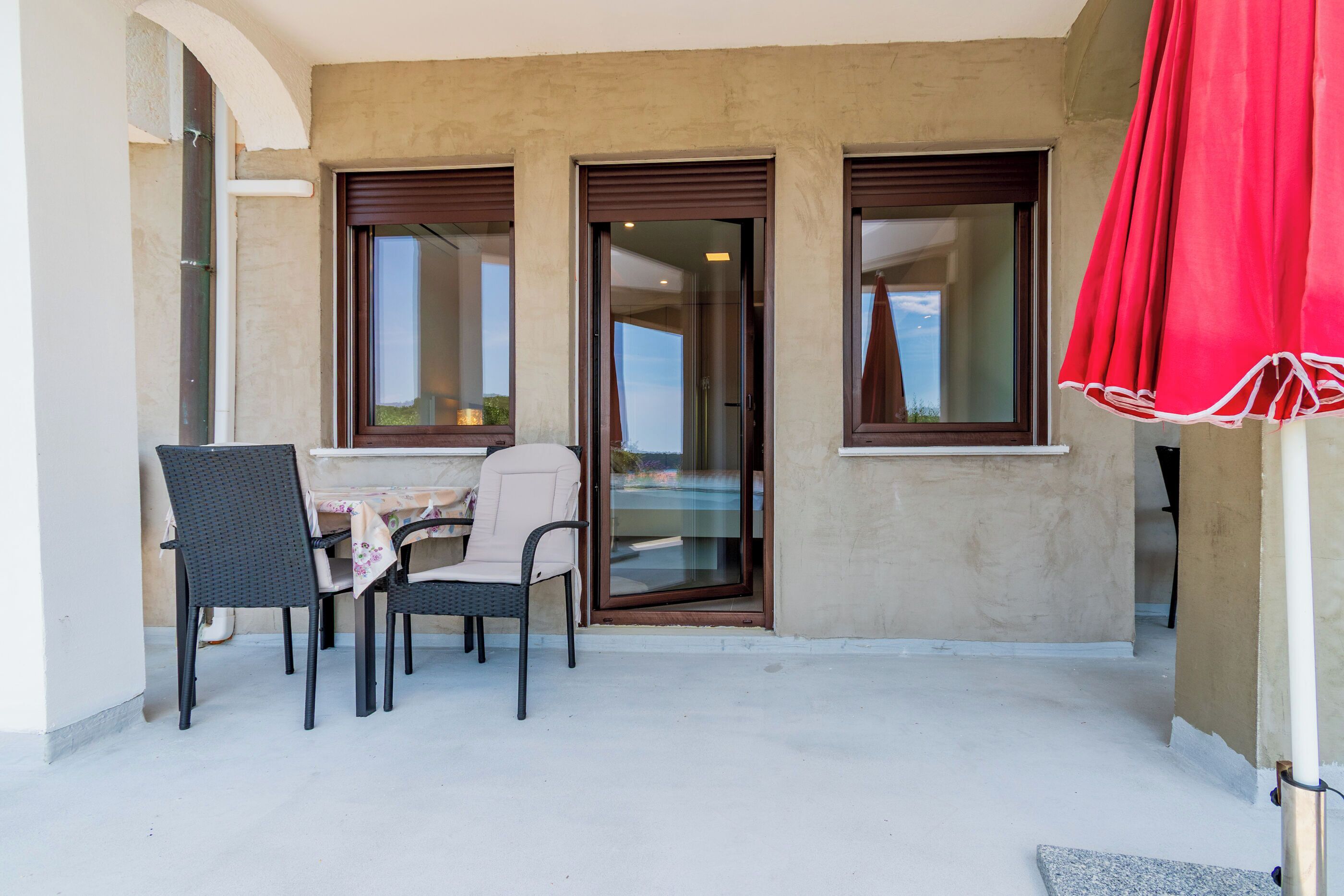 A balcony with a table and chairs, a sliding glass door, and a red curtain.