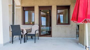 A balcony with a table and chairs, a sliding glass door, and a red curtain.