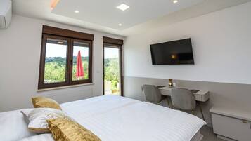 A hotel room with a large bed, a desk, a chair, a TV, and a window with a view.