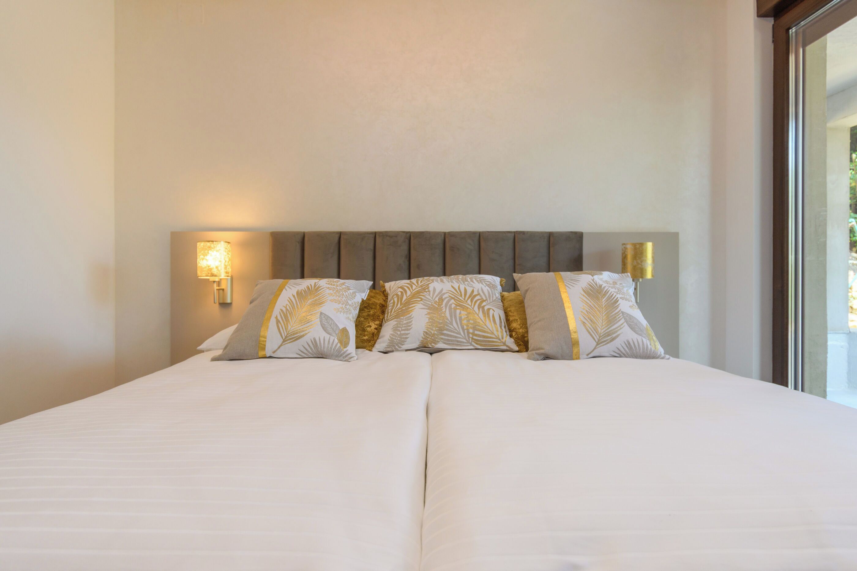 Una cama grande con cabecera, varias almohadas e iluminación en la pared.