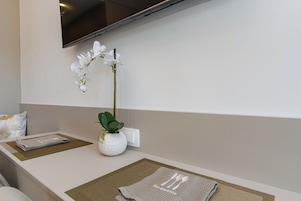 Un área de recepción limpia y moderna, con un televisor de pantalla plana en la pared, un jarrón blanco con una orquídea y un menú doblado sobre un posavasos.