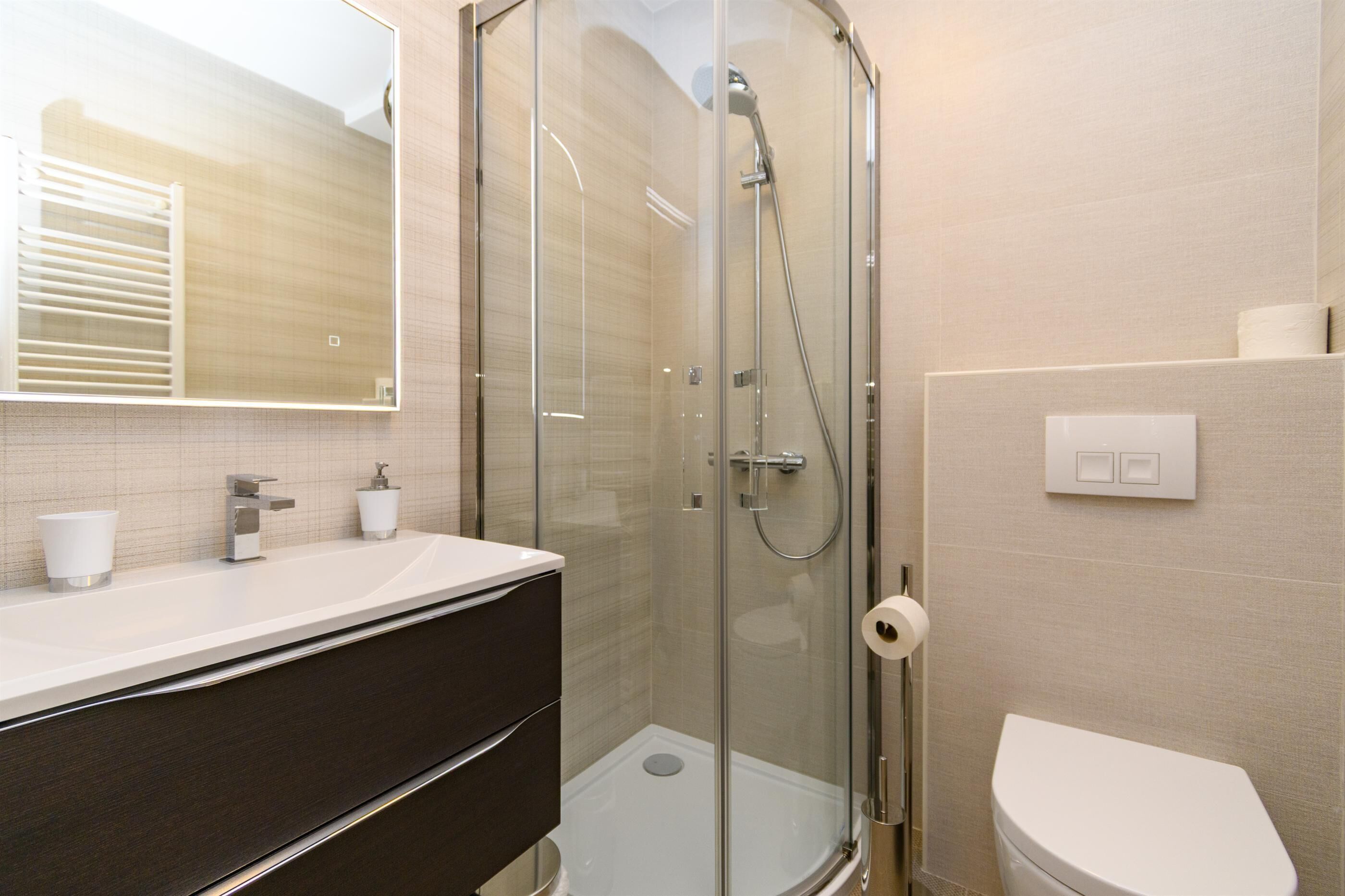 Un baño moderno con ducha envuelta en vidrio, un lavabo blanco con espejo y un inodoro.