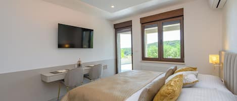 A bedroom with a bed, a desk, a chair, a TV, and a window with a view.