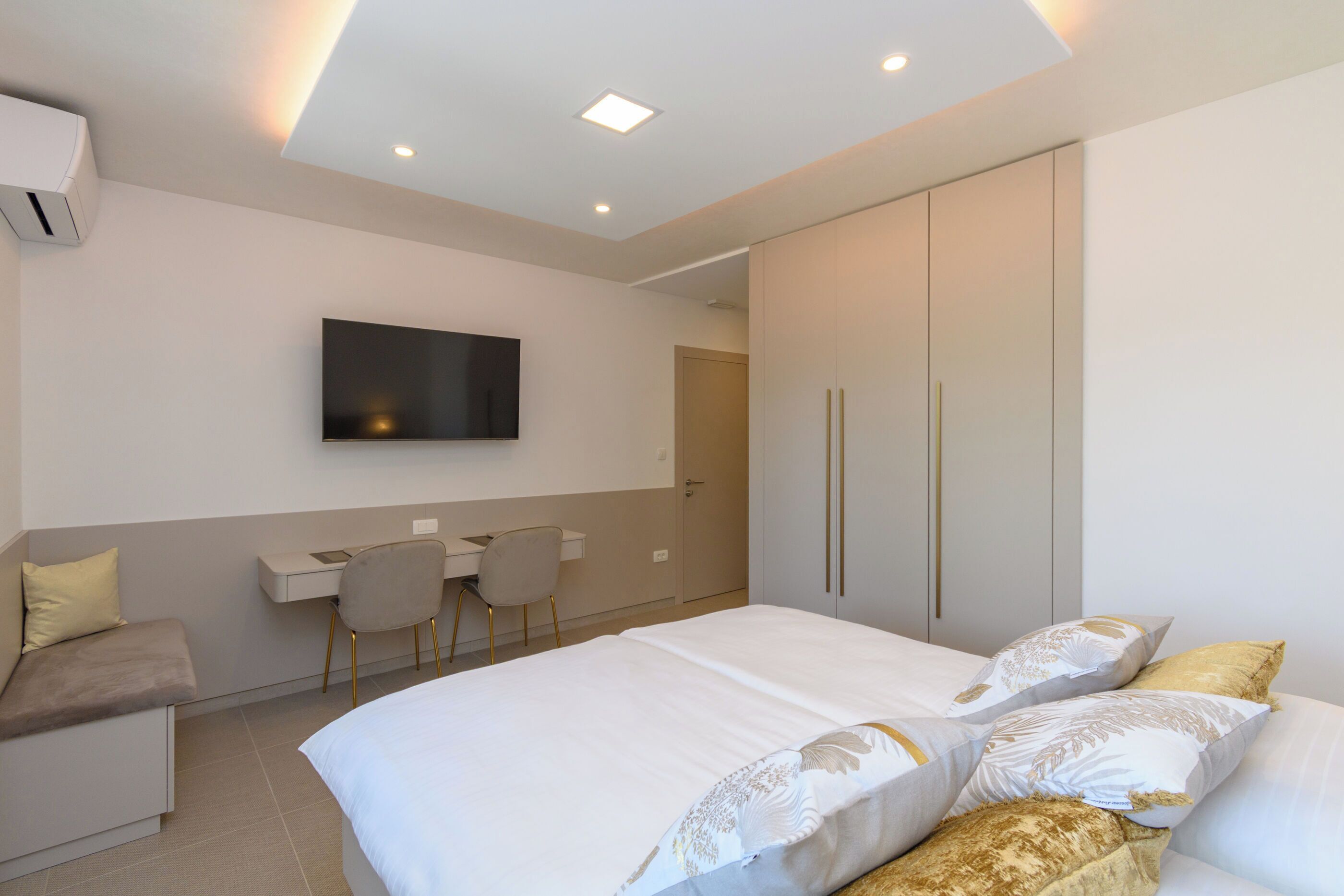 A modern bedroom with a bed, a desk, a chair, and a TV mounted on the wall.