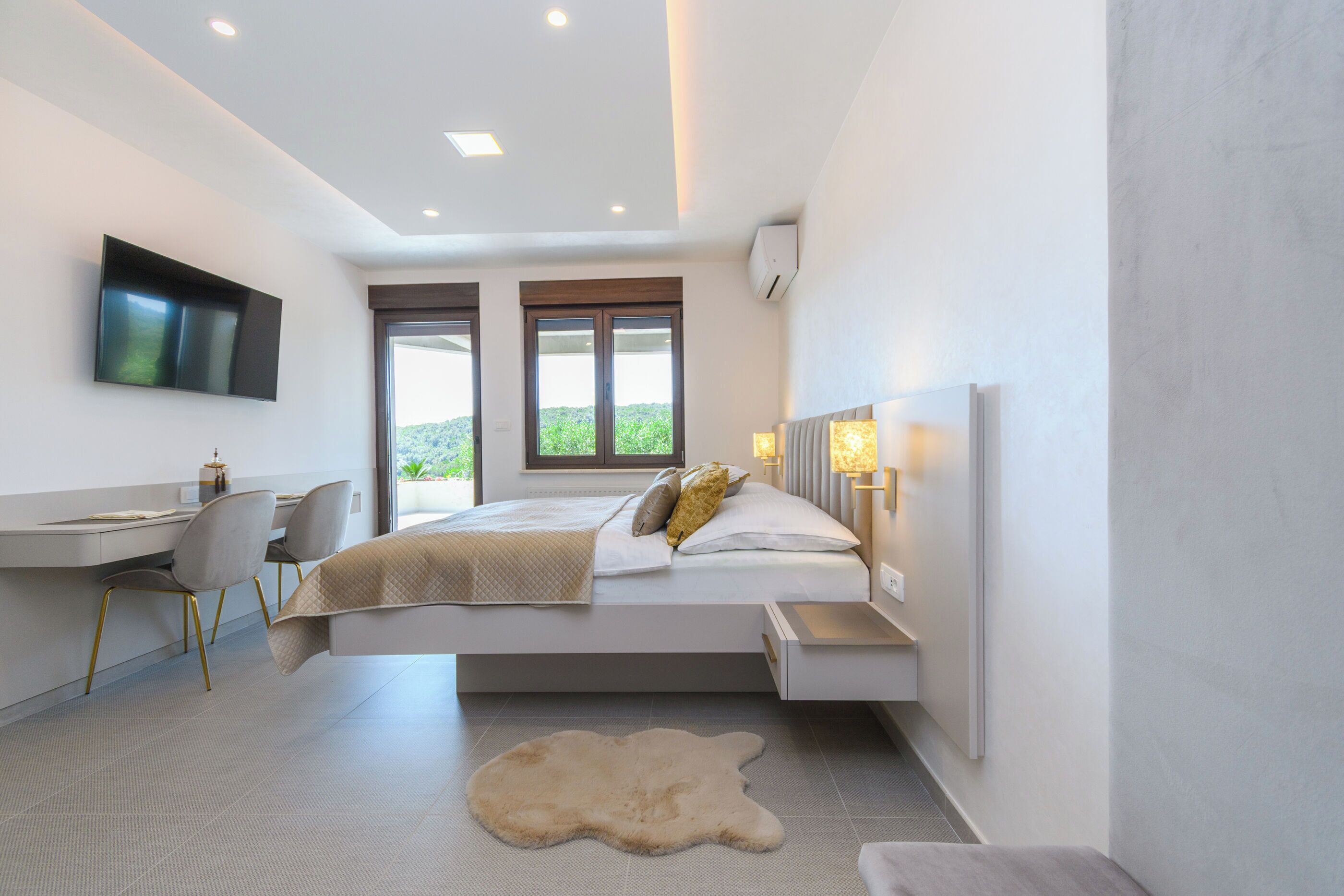 A modern bedroom with a bed, desk, and chair, a mounted TV, and a large window.