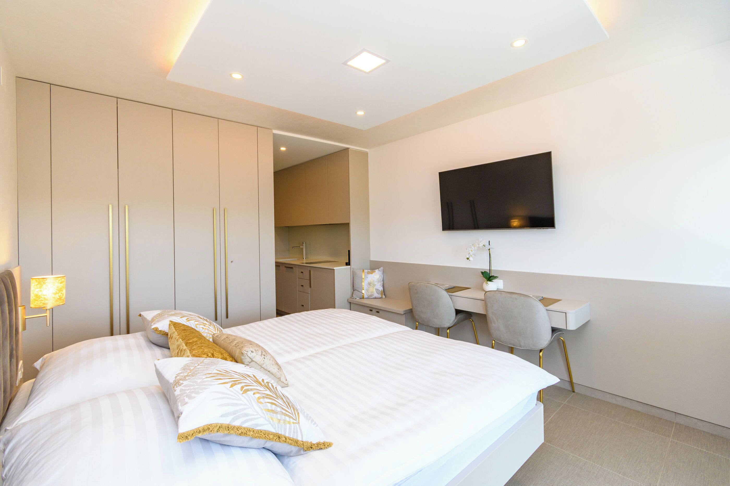 A modern hotel room with a large bed, a desk, a chair, and a TV mounted on the wall.