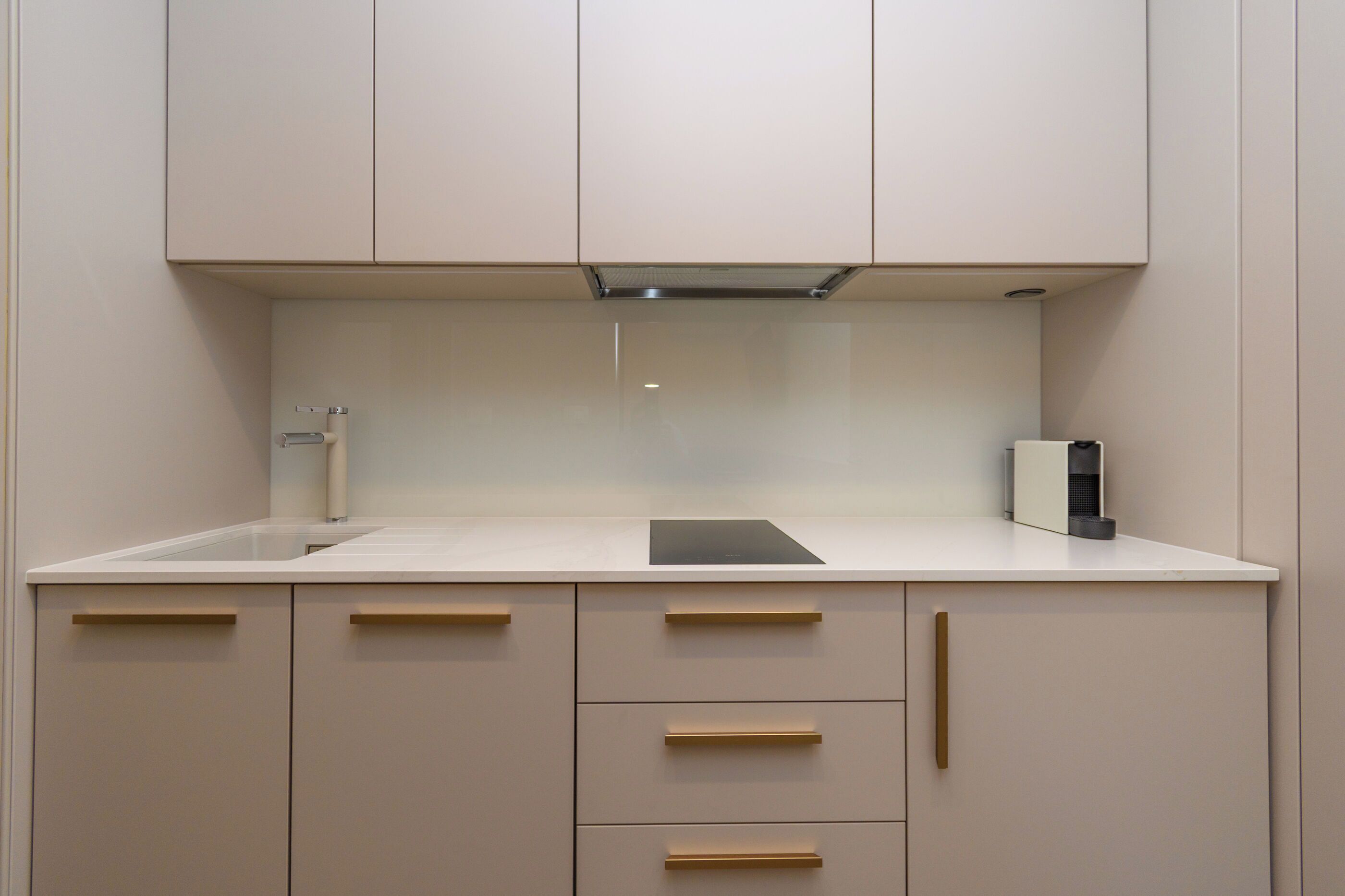 Une cuisine moderne avec un plan de travail blanc, des armoires de couleur beige et une hotte intégrée.