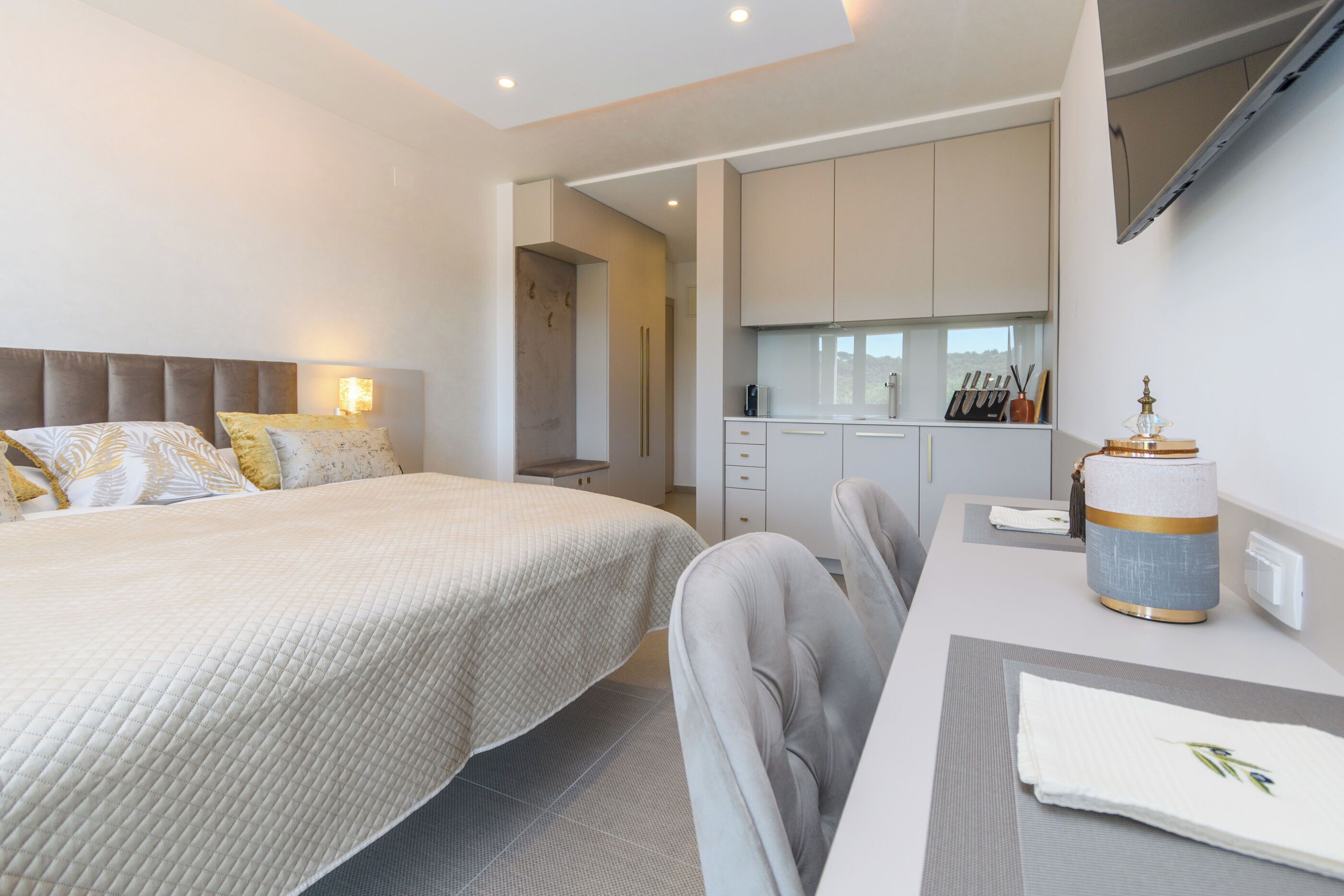 Een moderne hotelkamer met een groot bed, een bureau, een stoel, een klein keukenhoekje en een badkamer zichtbaar door een open deur.