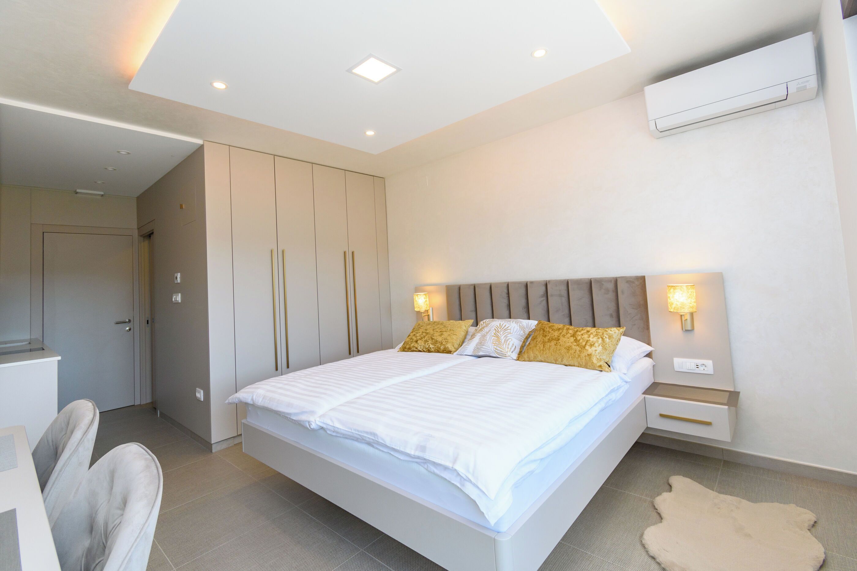 A modern bedroom with a large bed, bedside tables, a wardrobe, and an air conditioning unit.