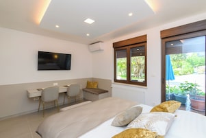 Un dormitorio moderno con cama, escritorio, dos sillas, televisor y ventana con vista a zonas verdes.