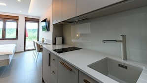 A modern kitchen with a large sink, a flat-screen TV mounted above the counter, and a dining area with a chair and table.