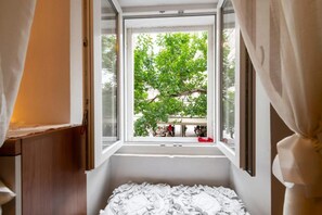 Ein Zimmer mit Fenster, einem Bett und Blick auf einen Baum sowie ein Gebäude.