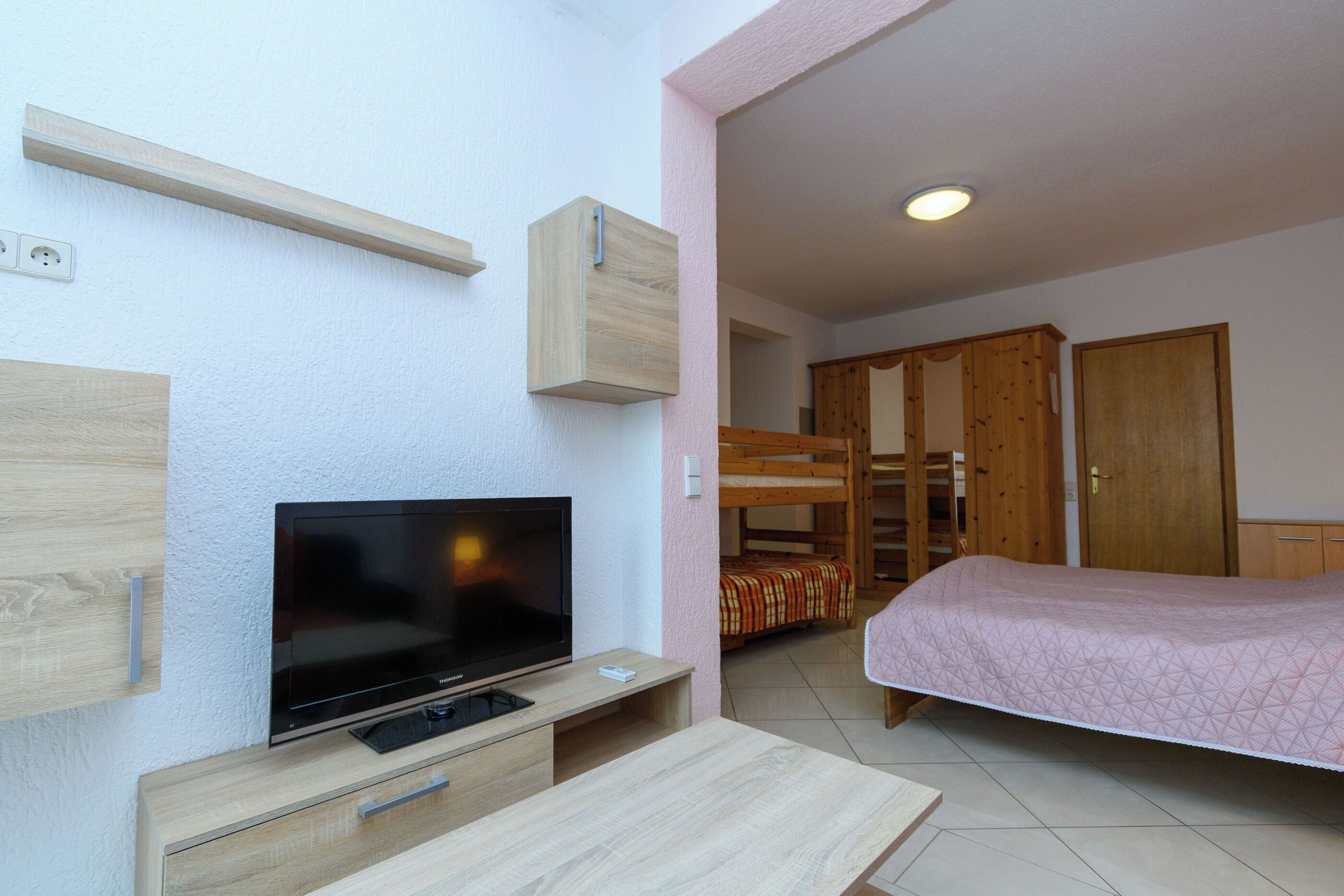 Ein Zimmer mit Fernseher, Holzm öbeln, einem Etagenbett und einem Kleiderschrank.