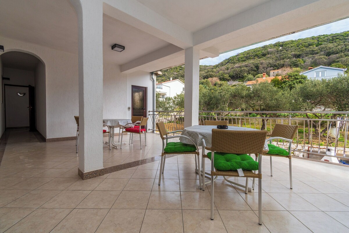 Un espacio al aire libre cubierto con una mesa, sillas, una puerta y vistas a una colina.