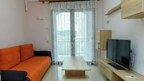 A living room with a sofa, a wooden coffee table, a television, and a window with curtains. - Apartments Maky (Rab)