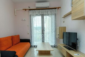 A living room with a sofa, a wooden coffee table, a television, and a window with curtains. - Apartments Maky (Rab)