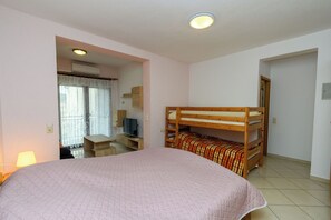 Ein Schlafzimmer mit Etagenbett, Schreibtisch mit Stuhl, Fernseher und einem Fenster mit Vorhängen.