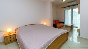 A bedroom with a bed, bedside tables, a nightstand, a window with curtains, and a view of the outdoors. - Apartments Maky (Rab)