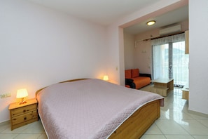 A bedroom with a bed, bedside tables, a nightstand, a window with curtains, and a view of the outdoors. - Apartments Maky (Rab)