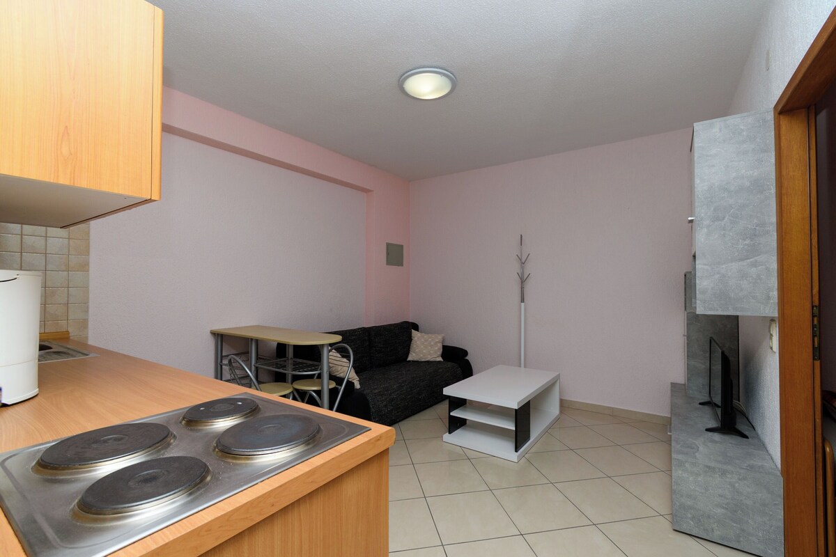 Cocina compacta con estufa, una pequeña mesa de comedor, un sofá y un televisor.