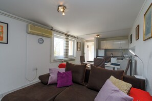 Ein gemütlicher Wohnbereich mit Sofa, Esstisch, Küchenzeile und einem Fenster mit Vorhängen.